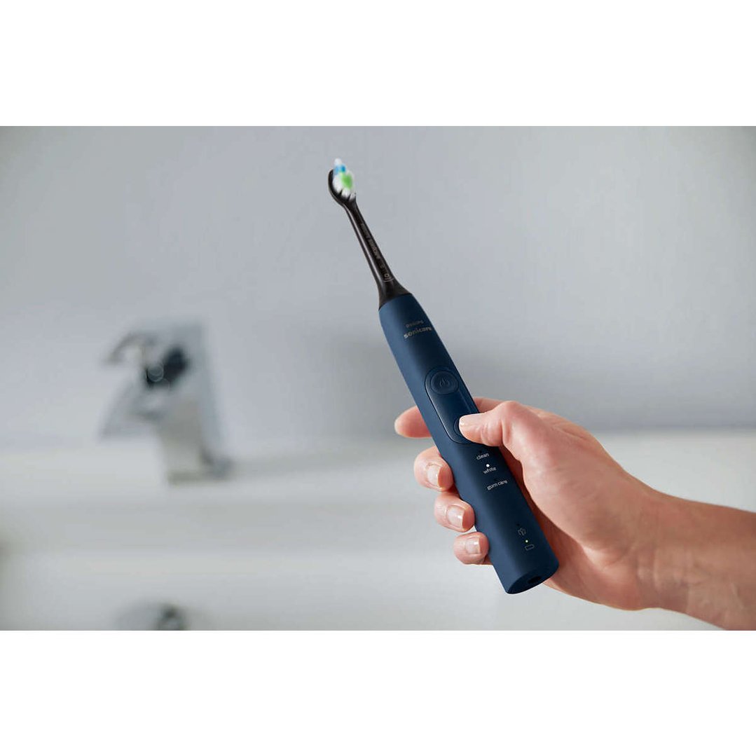 Hand holding a blue Philips Sonicare electric toothbrush over a bathroom sink