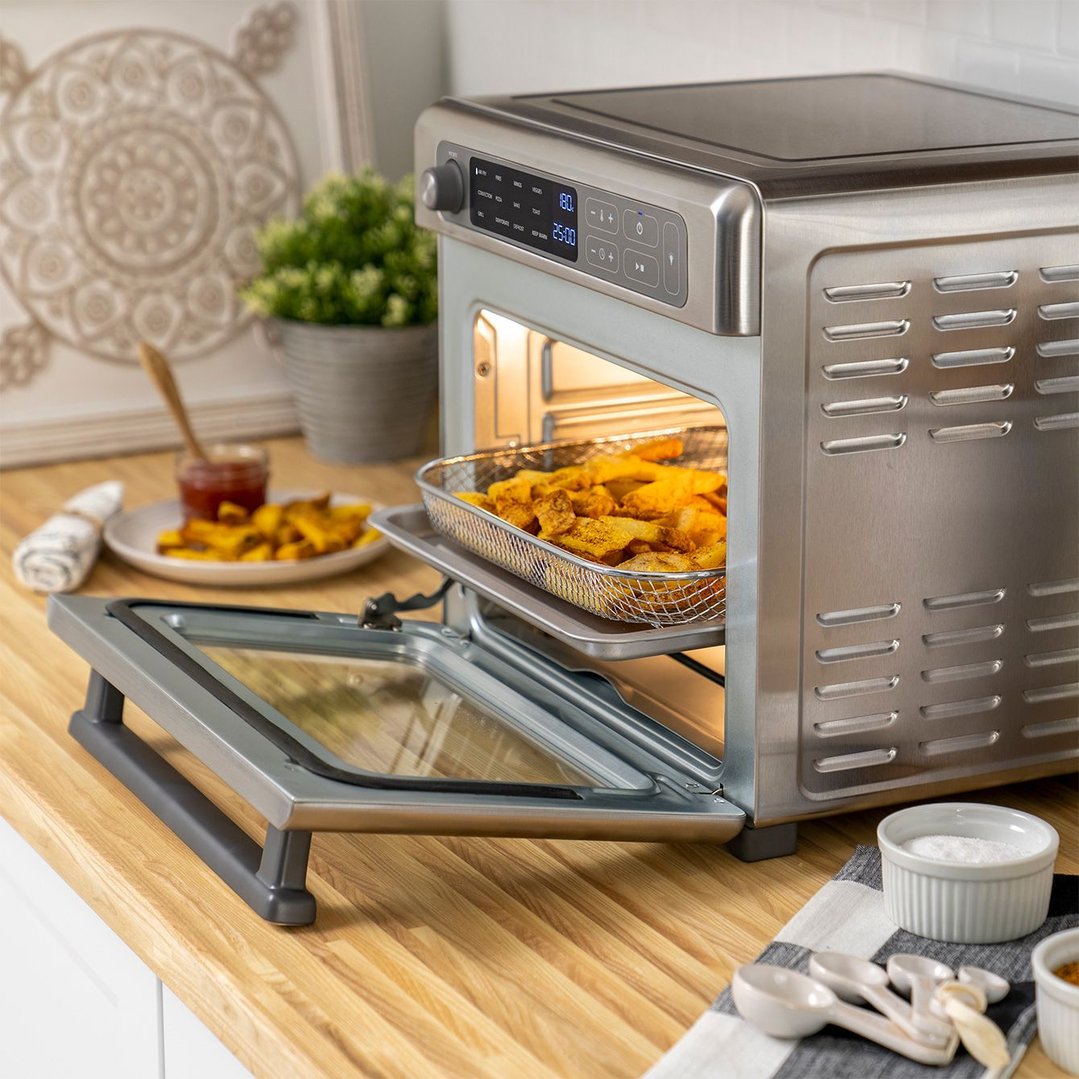Air fryer oven with fries cooking inside, on a wooden kitchen counter
