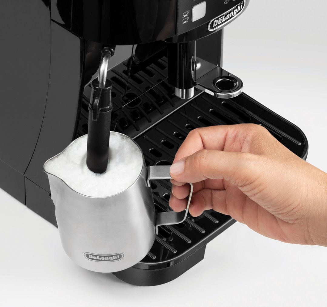 Hand holding a milk frothing jug under the steam wand of a coffee machine