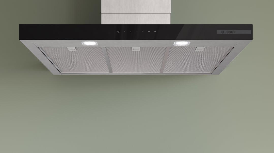 A stainless steel look rangehood with lights on, mounted on a green wall