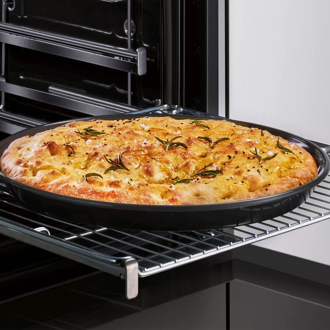 Pizza tray with focaccia bread inside an oven on a rack