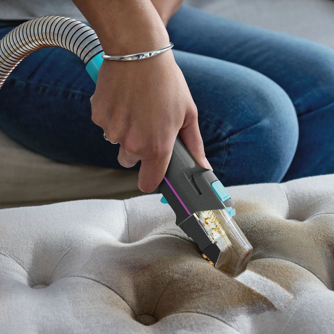 Hand using a vacuum cleaner to clean a stained upholstered surface