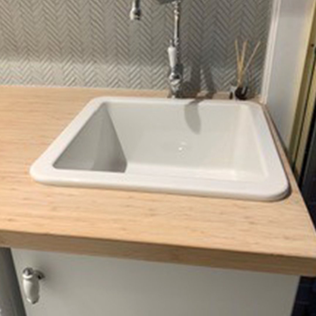 White fireclay sink inset into a wooden countertop with a patterned backsplash
