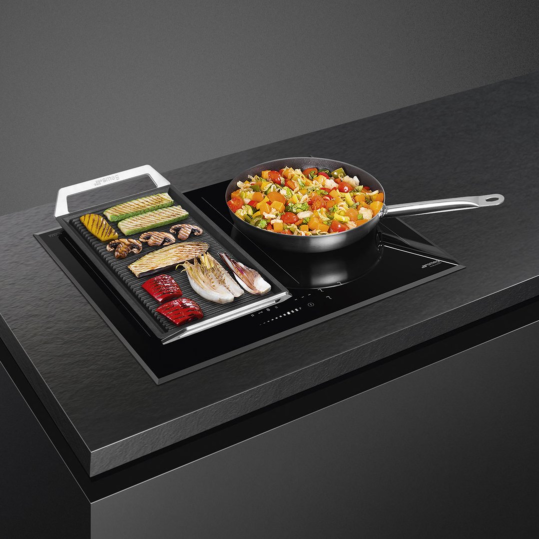 SMEG induction hob with a grill plate and a pan of vegetables on a dark countertop
