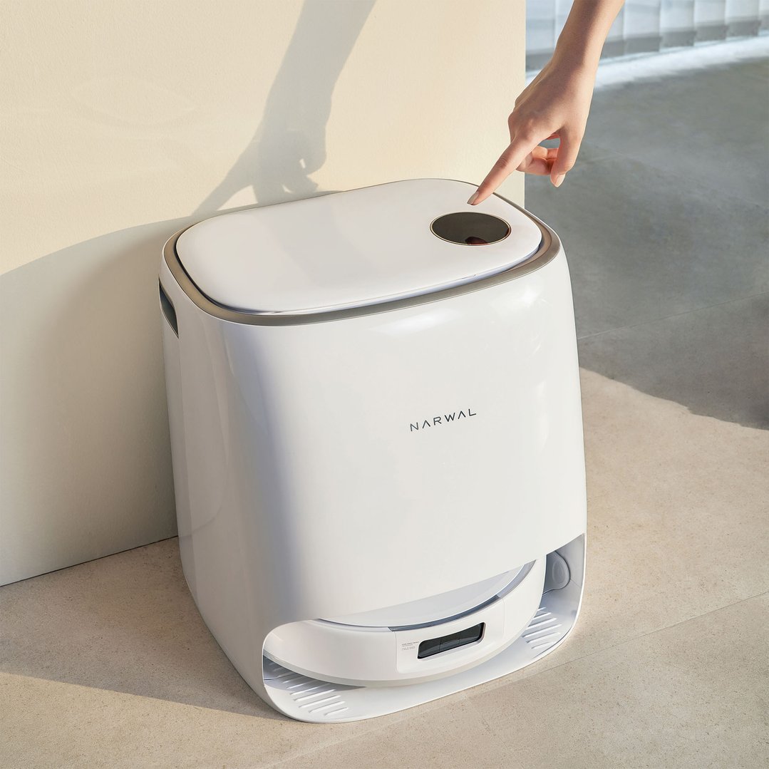 A hand pressing the power button on a white NARWAL robotic vacuum and mop