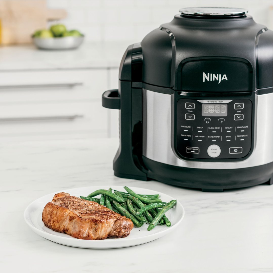 Ninja multi cooker on a kitchen counter with a plate of steak and green beans
