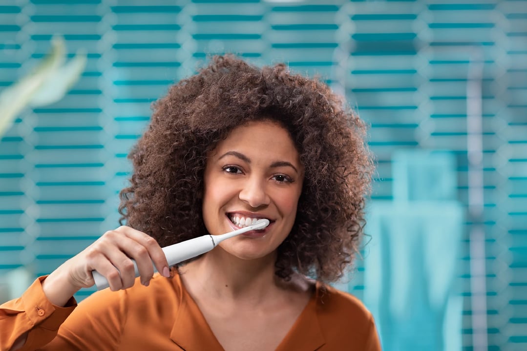 Woman brushing her teeth with a white electric toothbrush in a bathroom