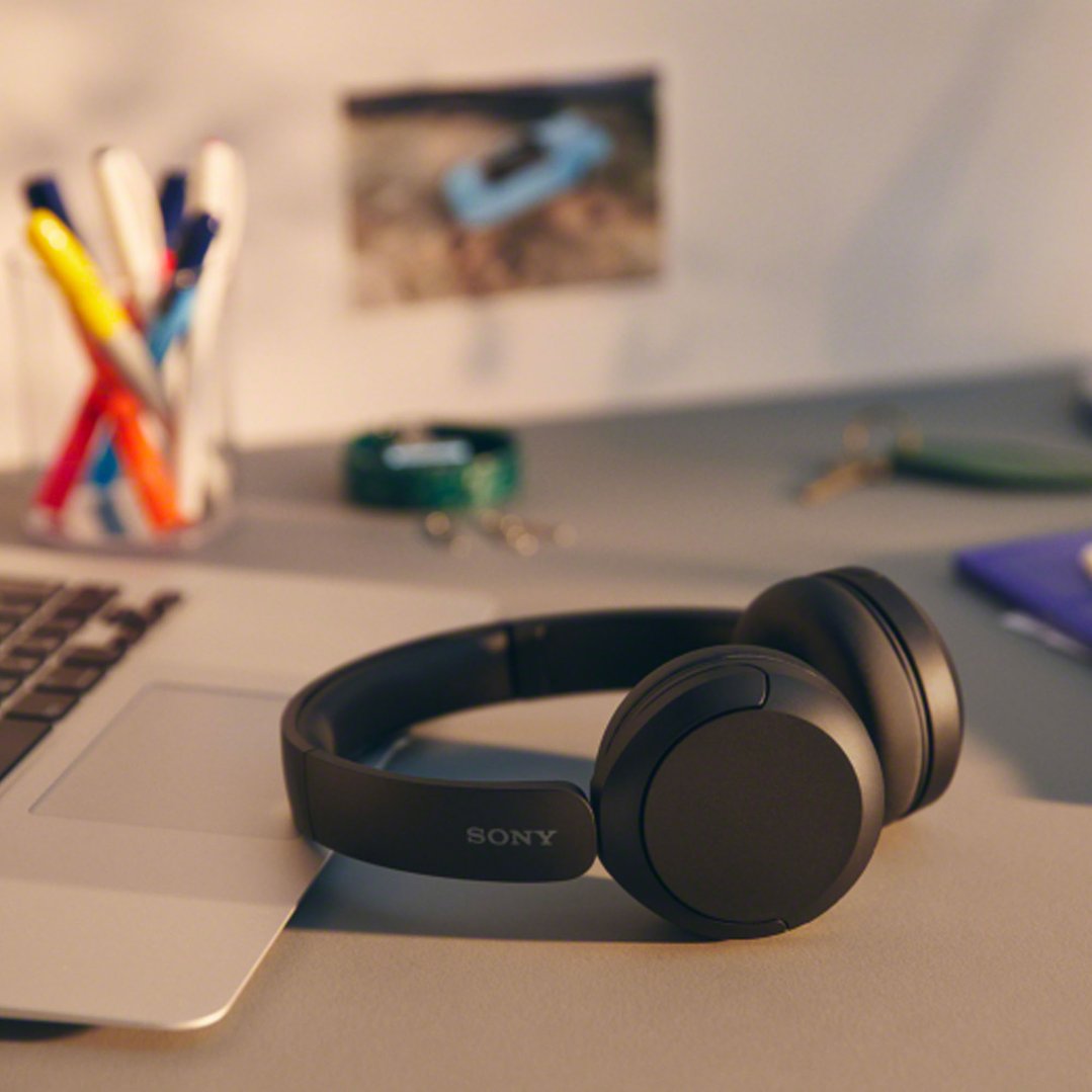 Black Sony wireless headphones on a desk next to a laptop and pens