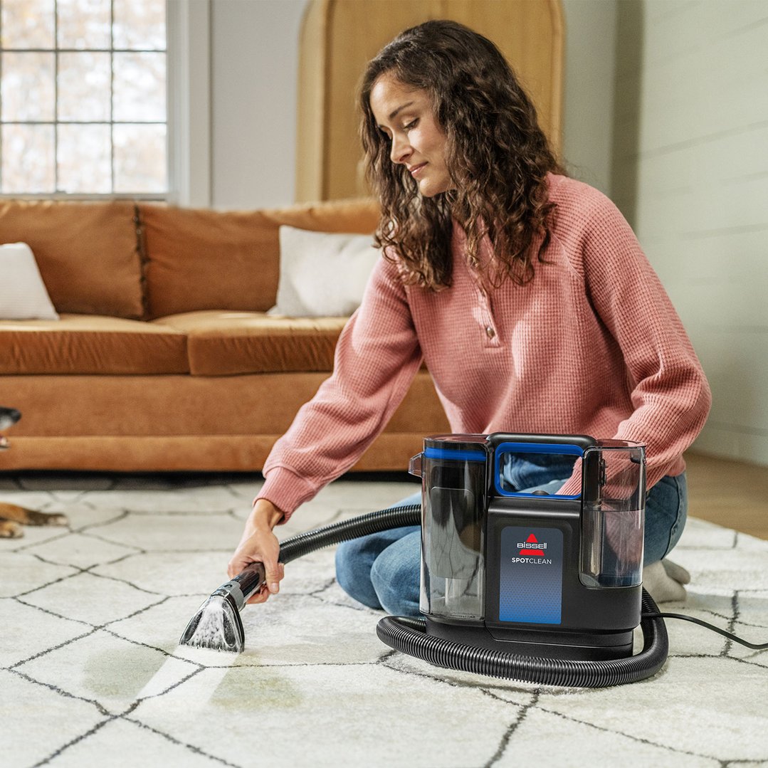 Woman cleaning a white patterned rug with a BISSELL SpotClean vacuum cleaner