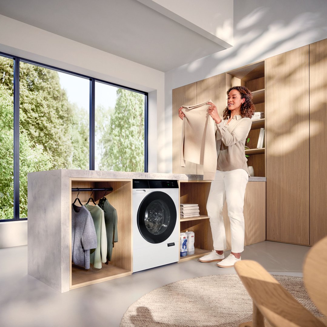 Woman holding a sweater next to a Miele front load washing machine