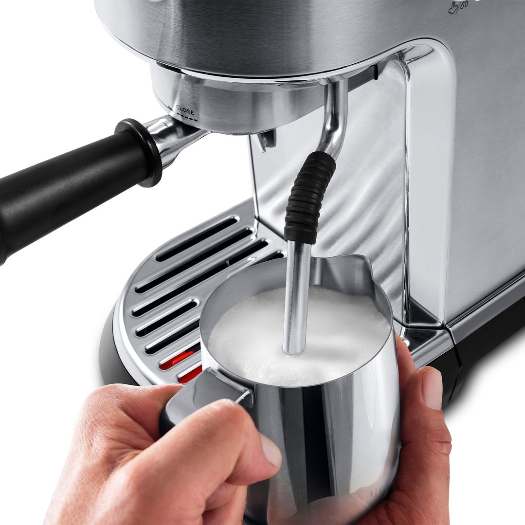 Hands holding a milk frothing pitcher under the steam wand of a coffee machine