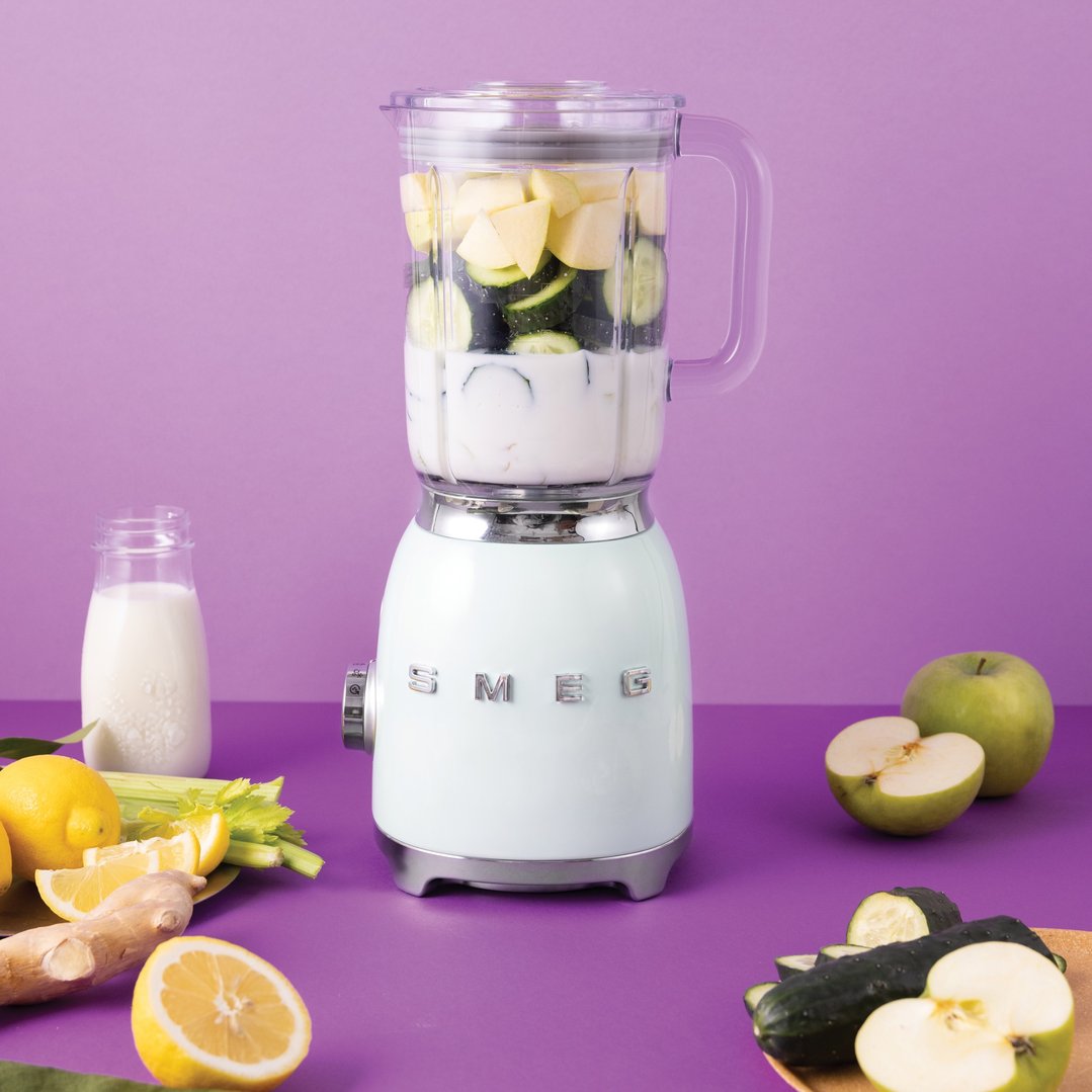 White blender with ingredients on a purple surface with other produce