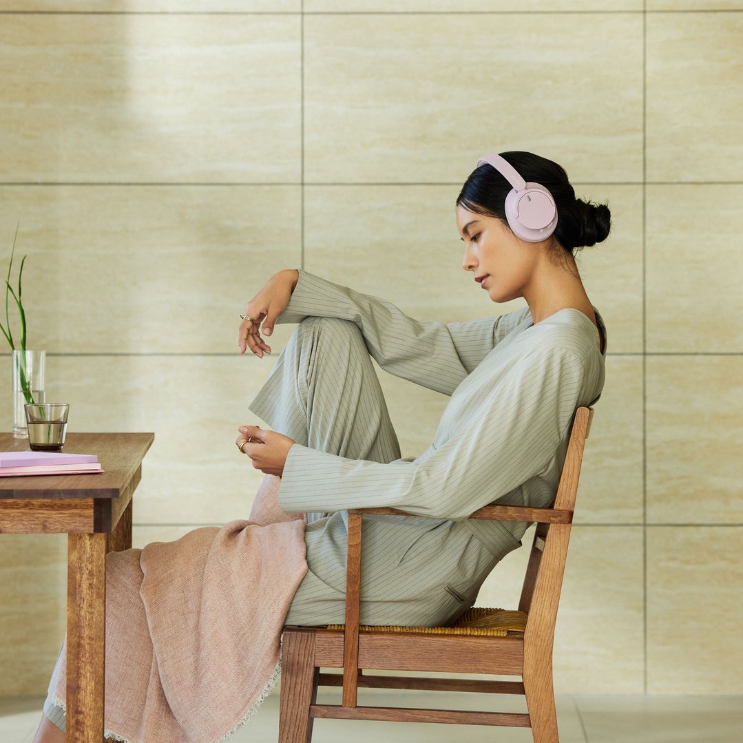Woman wearing pink SONY Wireless Noise Cancelling Headphones, sitting in a wooden chair