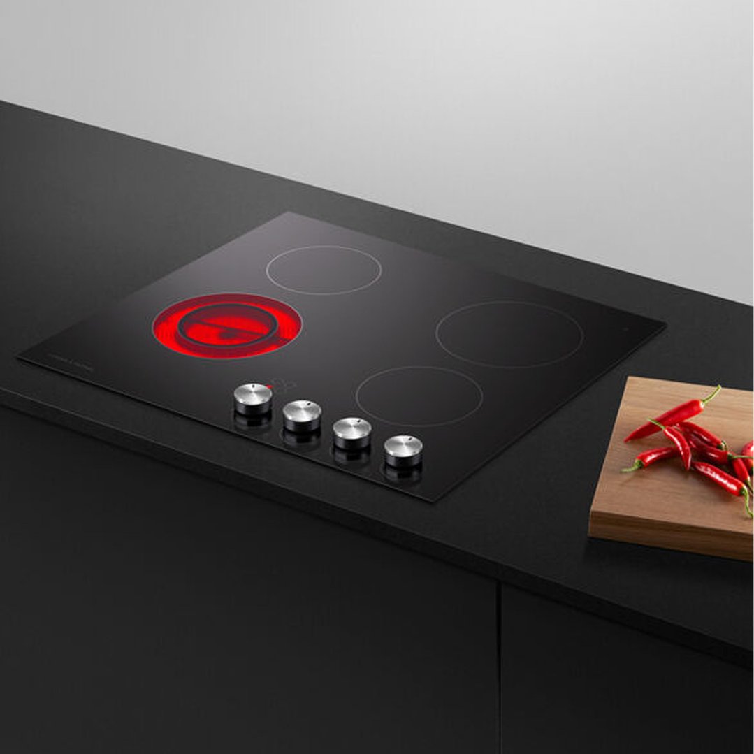 Black electric cooktop with one red-hot element, on a dark countertop with chilies