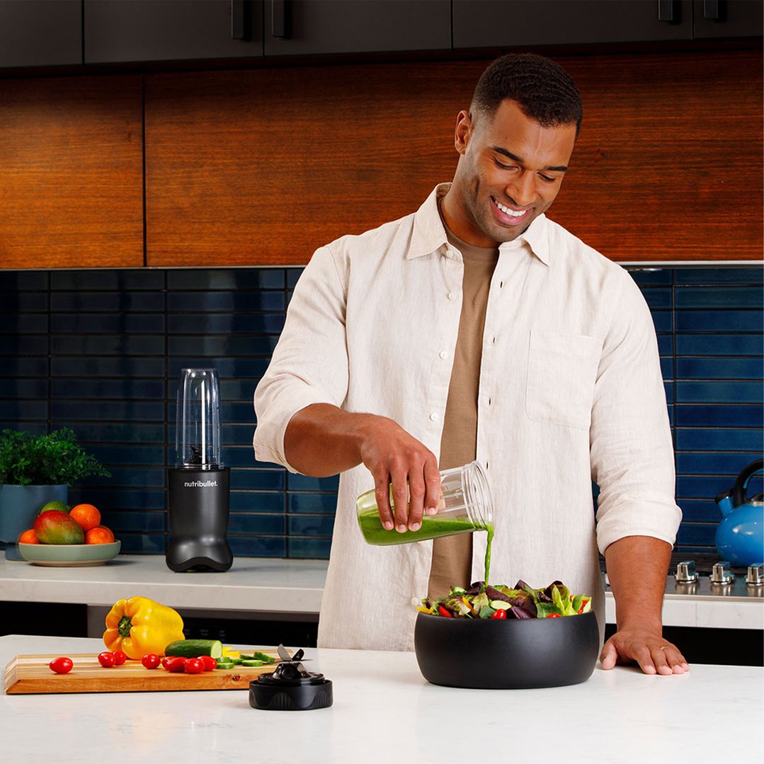 Man pouring green smoothie from a blender cup into a salad bowl