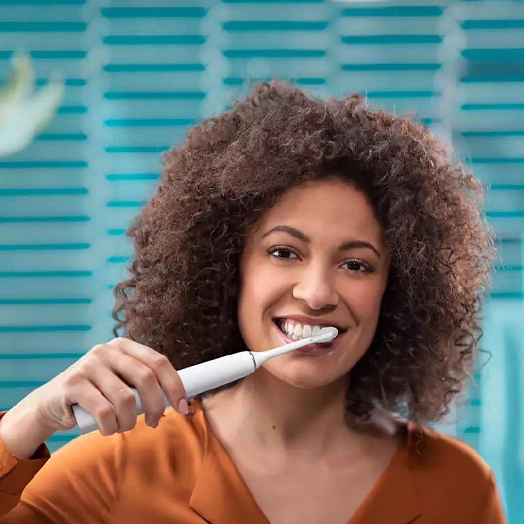 Smiling woman brushing her teeth with a white Sonicare DiamondClean 9000 electric toothbrush