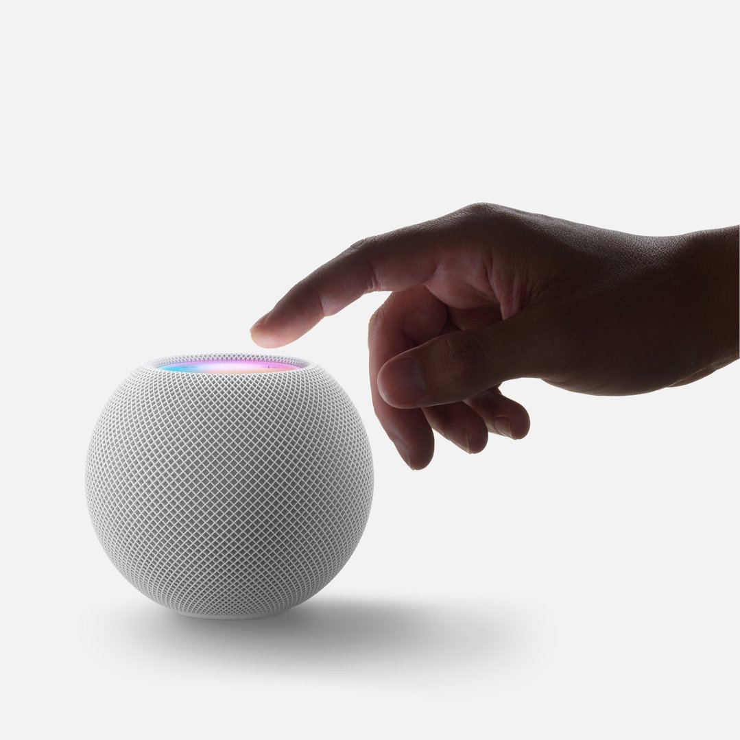 Hand touching the top of a white HomePod mini smart speaker with colorful lights