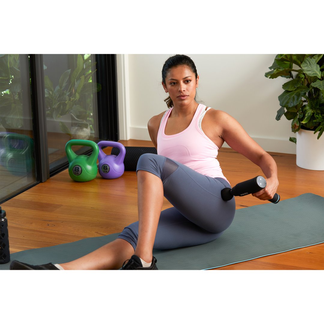 Woman sitting on a yoga mat using a percussion massager on her leg