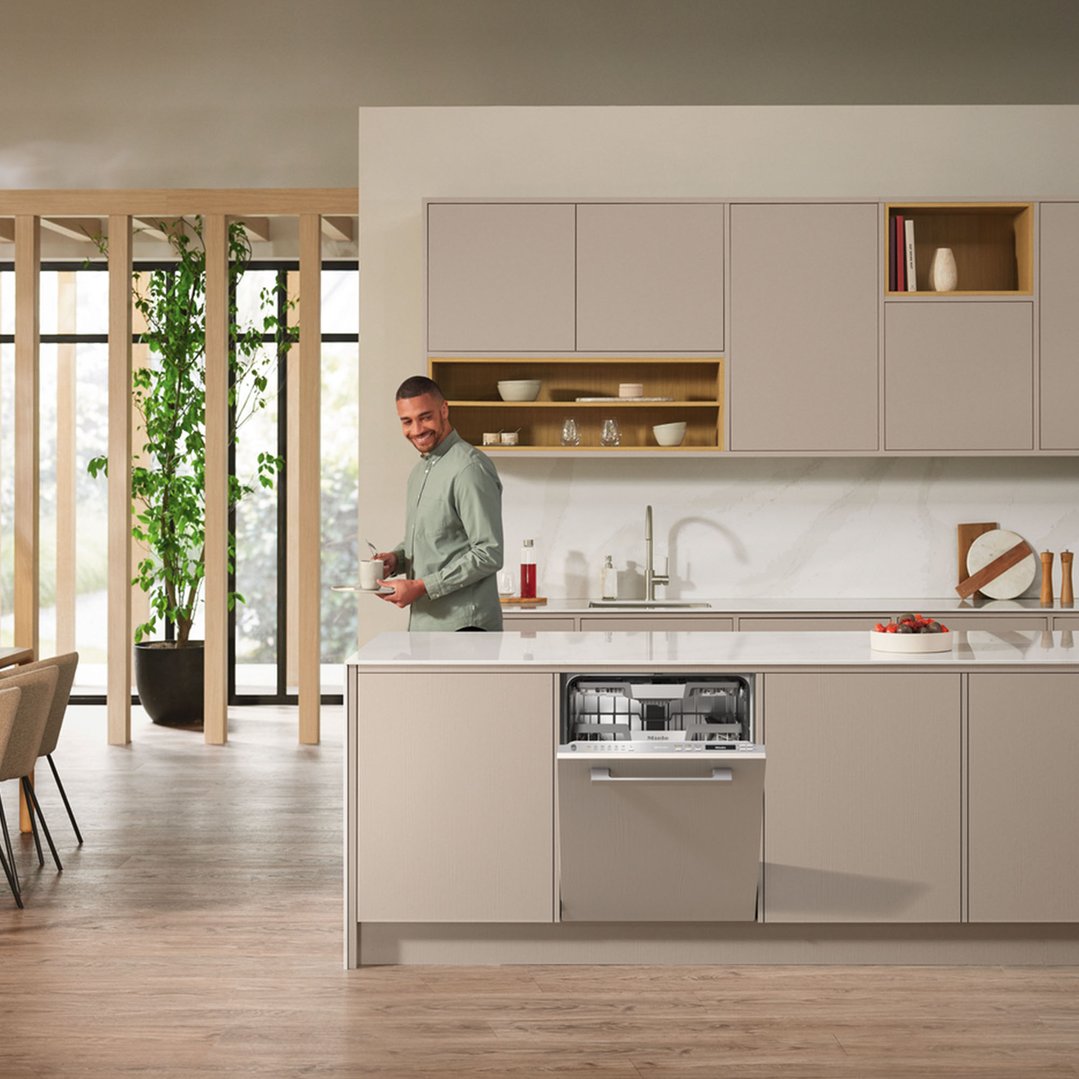 Man holding a tray with a cup in a modern kitchen with an open dishwasher