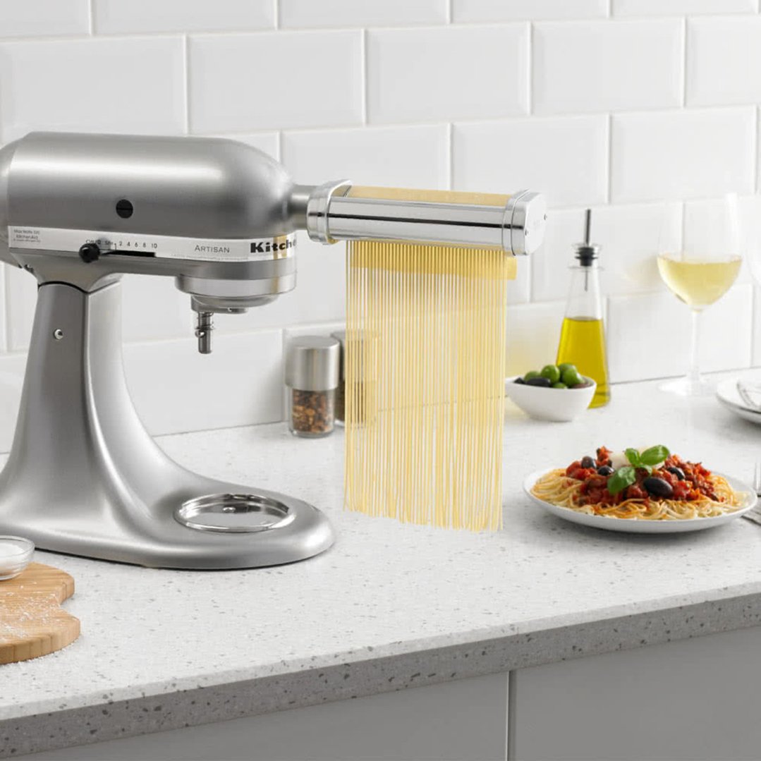 KitchenAid stand mixer with pasta roller attachment making spaghetti in a kitchen setting