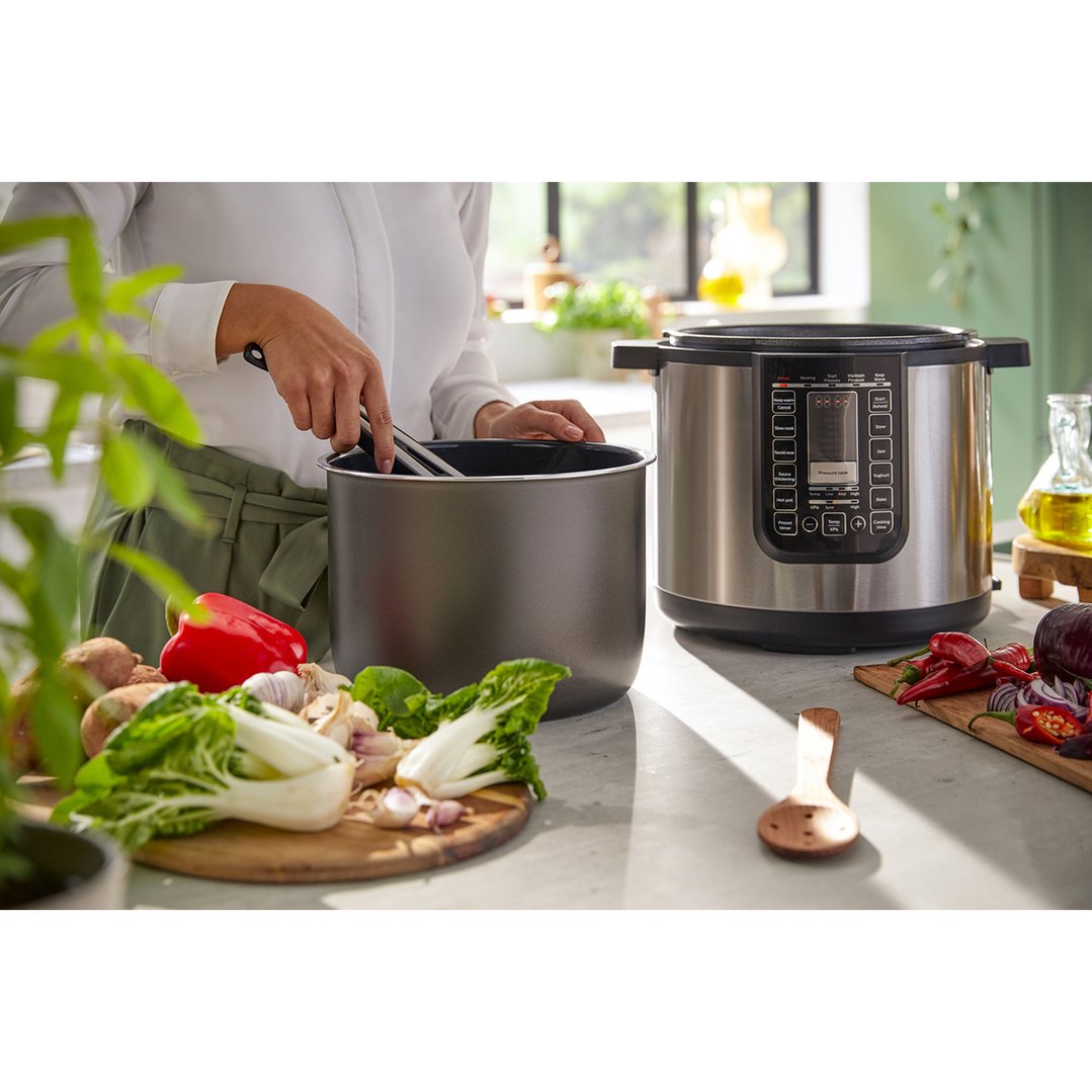 Woman preparing vegetables next to a Philips All-in-One Cooker on a kitchen counter