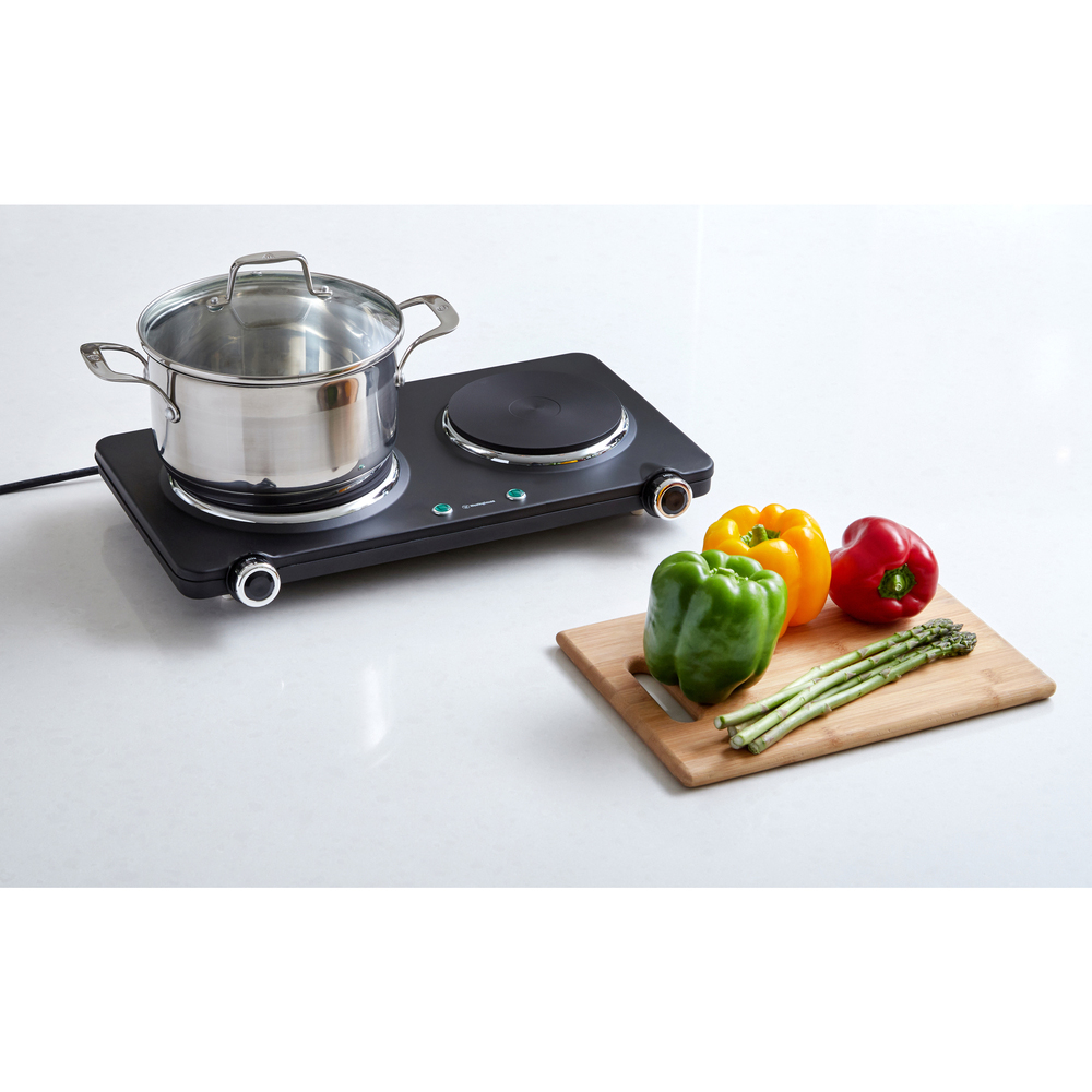 Double electric hotplate with a pot and vegetables on a white countertop
