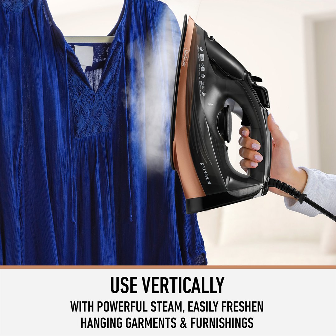 Hand holding a Sunbeam iron, steaming a blue garment hanging vertically