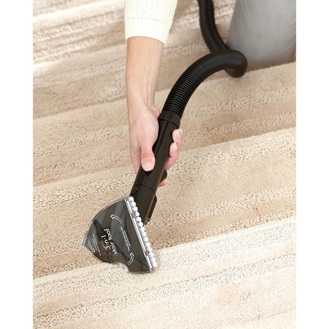 Hand using a vacuum cleaner attachment to clean carpeted stairs