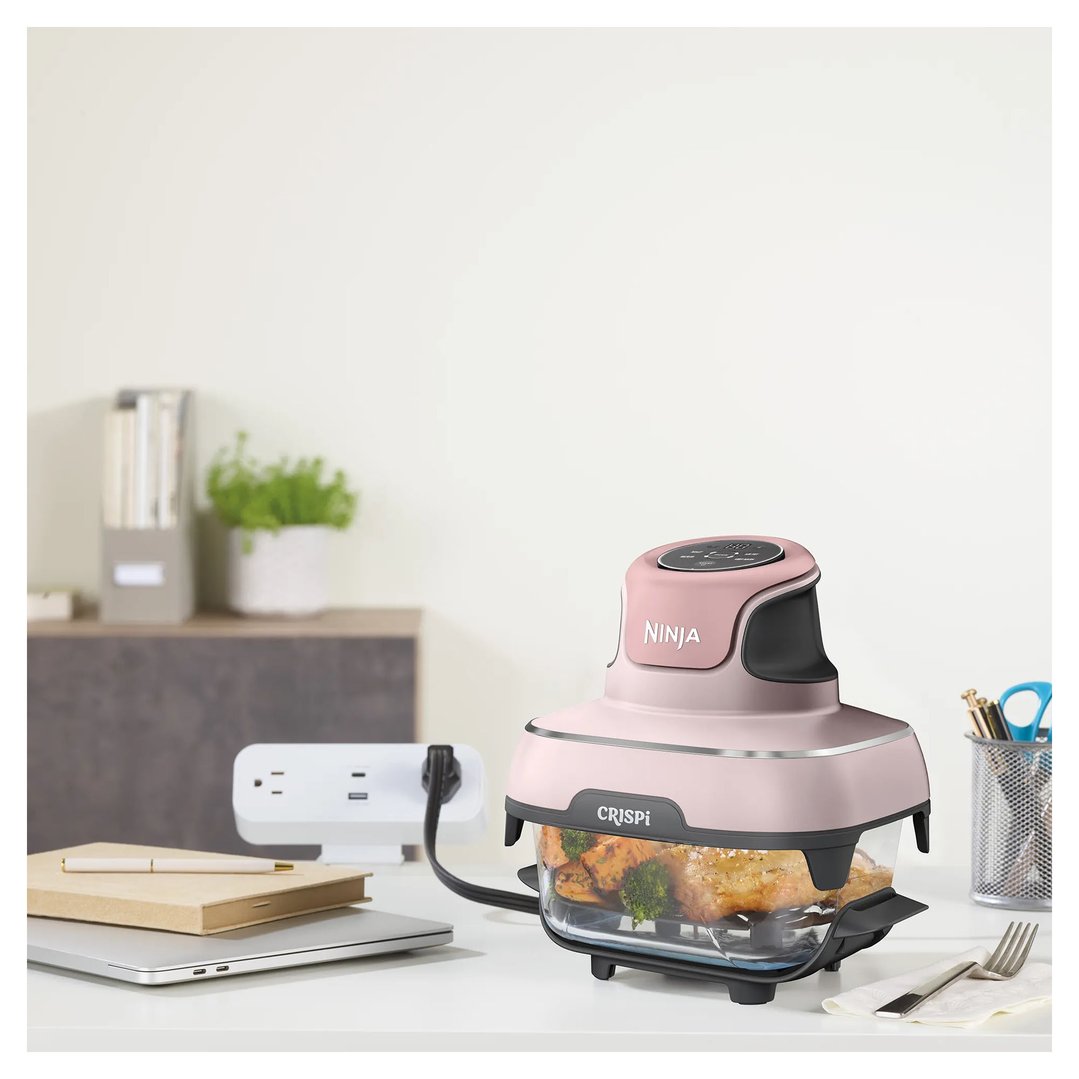 Pink Ninja Crispi air fryer cooking food on a white desk with a laptop