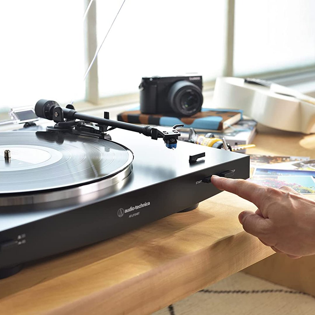 Hand pressing start button on black Audio-Technica turntable on wooden surface