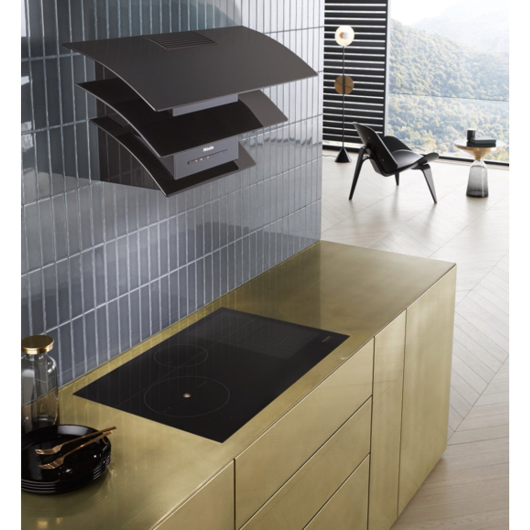 Black rangehood and cooktop in a modern kitchen with gold cabinetry
