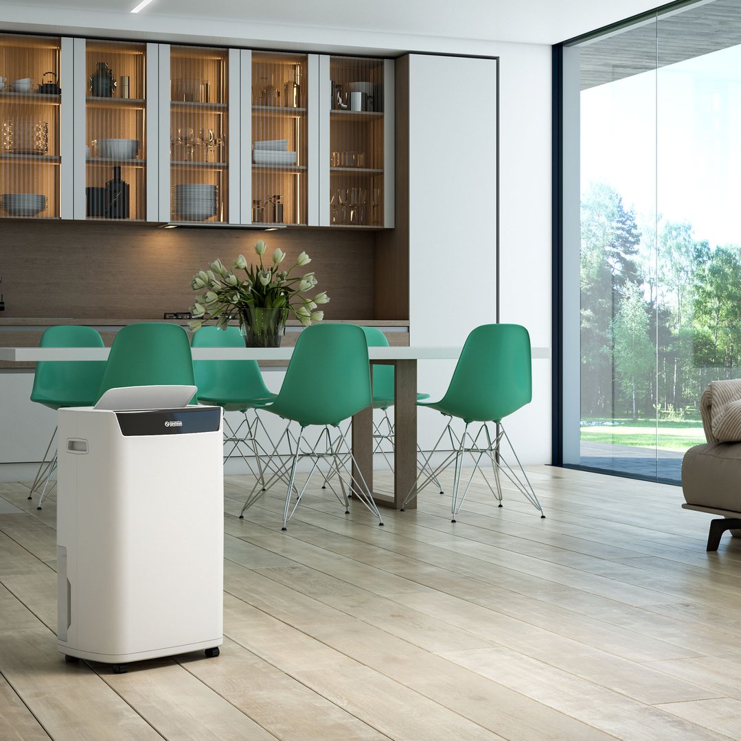 A white dehumidifier in a modern kitchen and dining area with green chairs