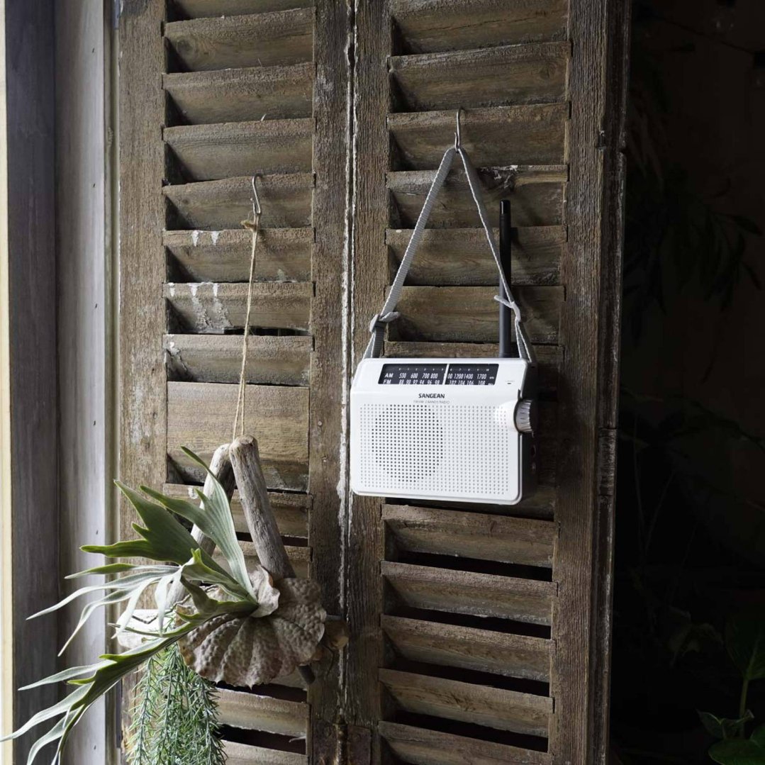 White portable radio hanging on a rustic wooden shutter with plants