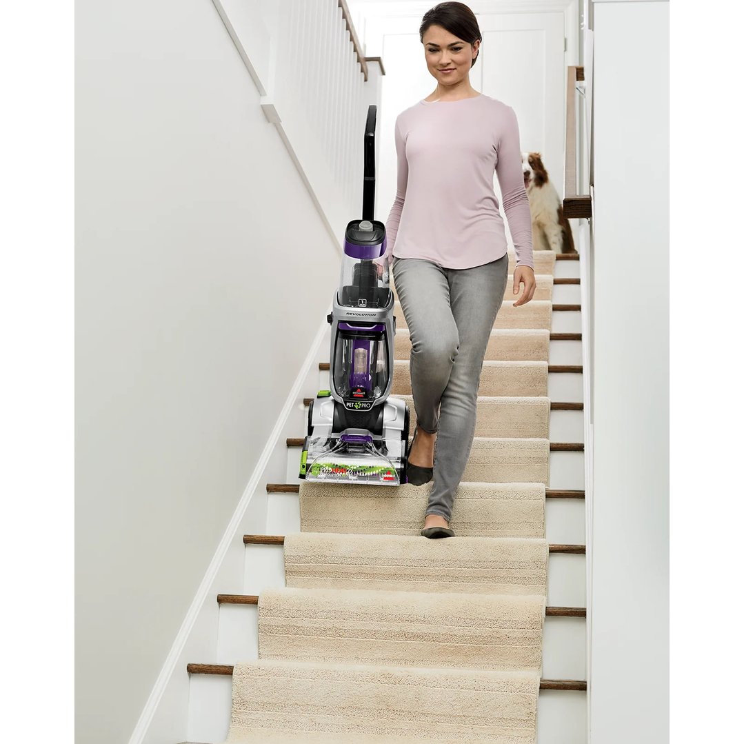 Woman carrying a BISSELL ProHeat 2X Revolution Pet Upright Carpet Washer down carpeted stairs