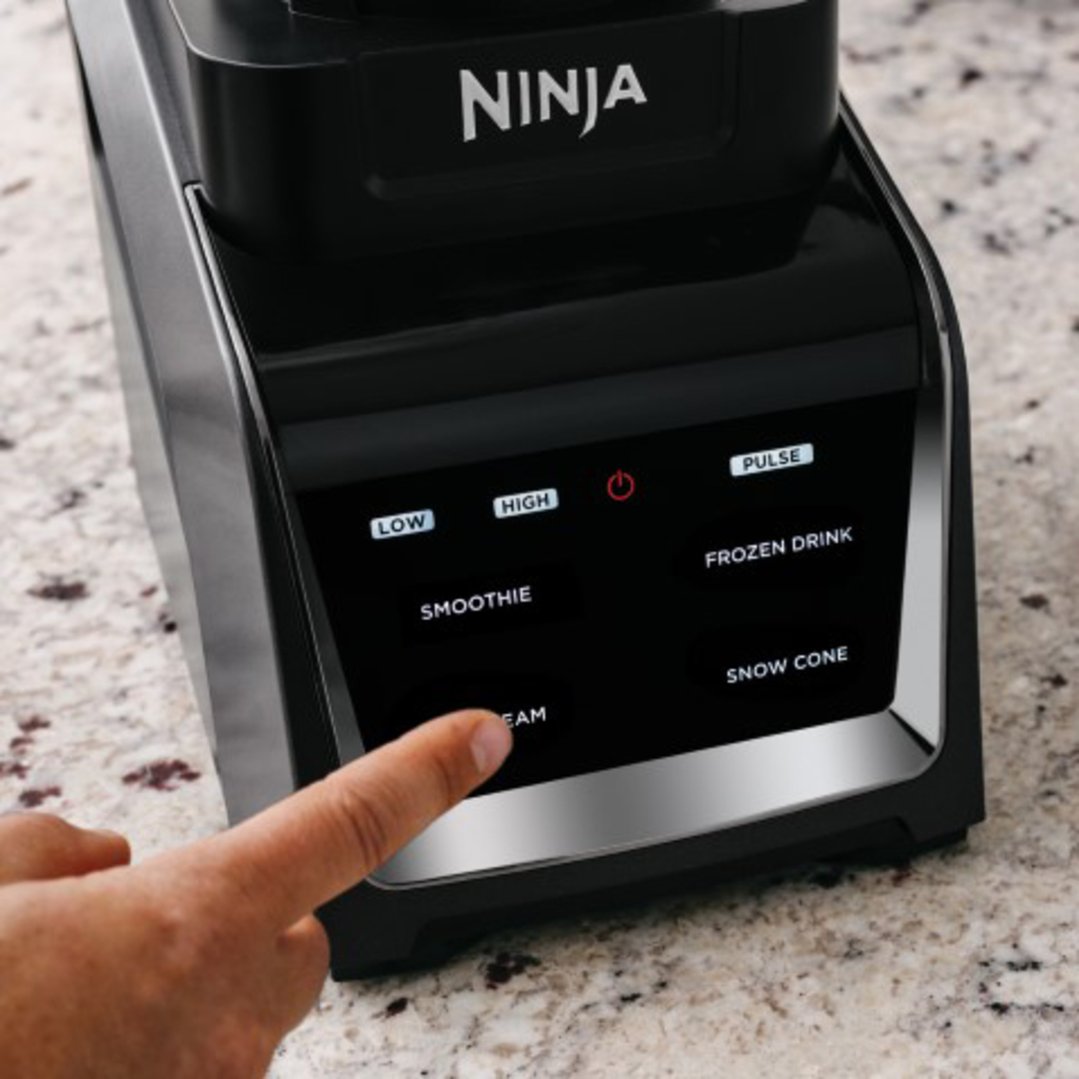 A hand pressing a button on the control panel of a Ninja blender