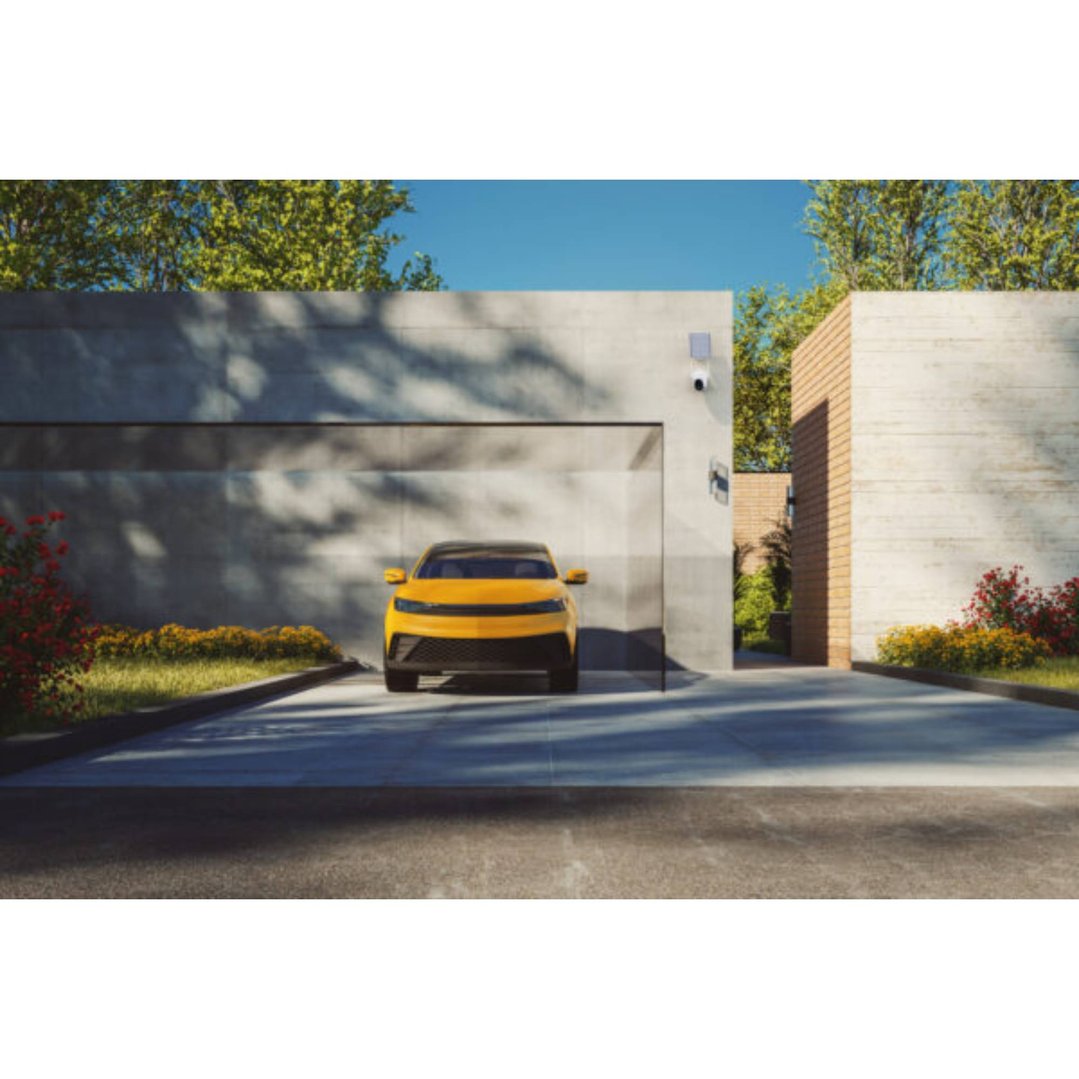 Security camera with solar panel mounted on a modern house wall above a car