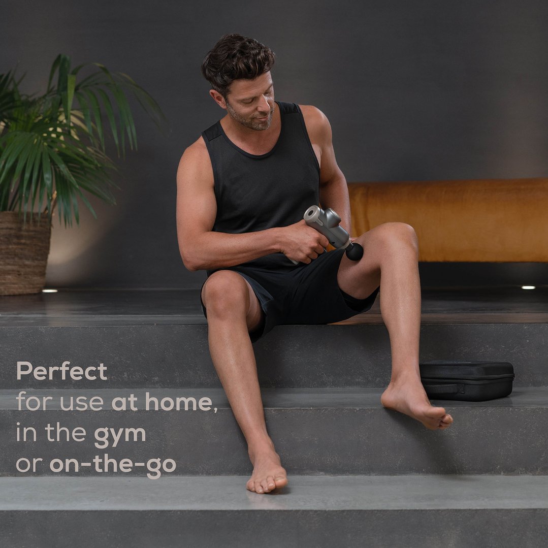 Man using a compact massage gun on his leg while sitting on steps