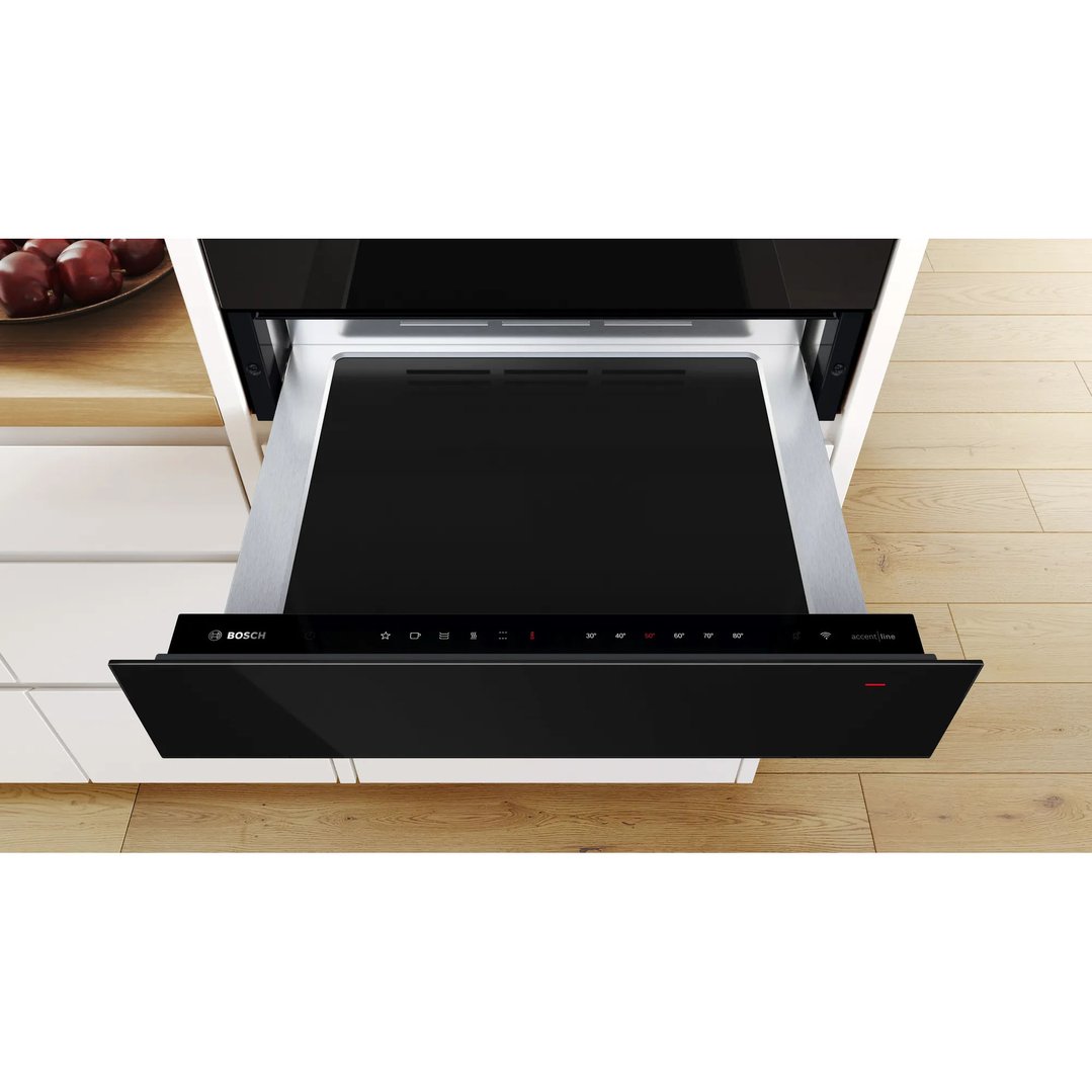 Black warming drawer pulled out in a kitchen setting with wooden floor