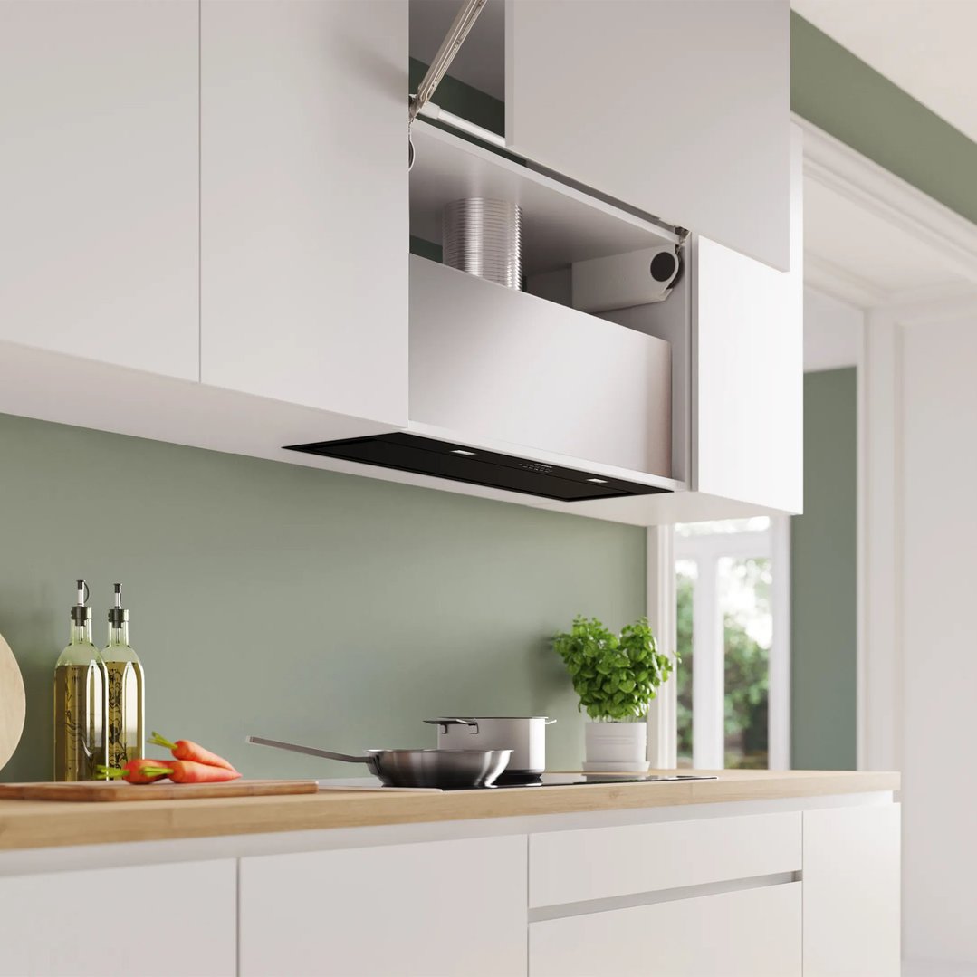 Integrated rangehood in a modern kitchen with white cabinets and green wall