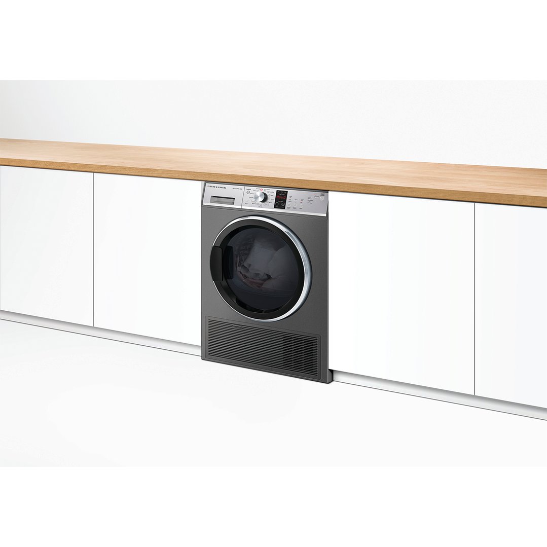 Dark grey heat pump dryer built into white cabinetry with a wooden countertop