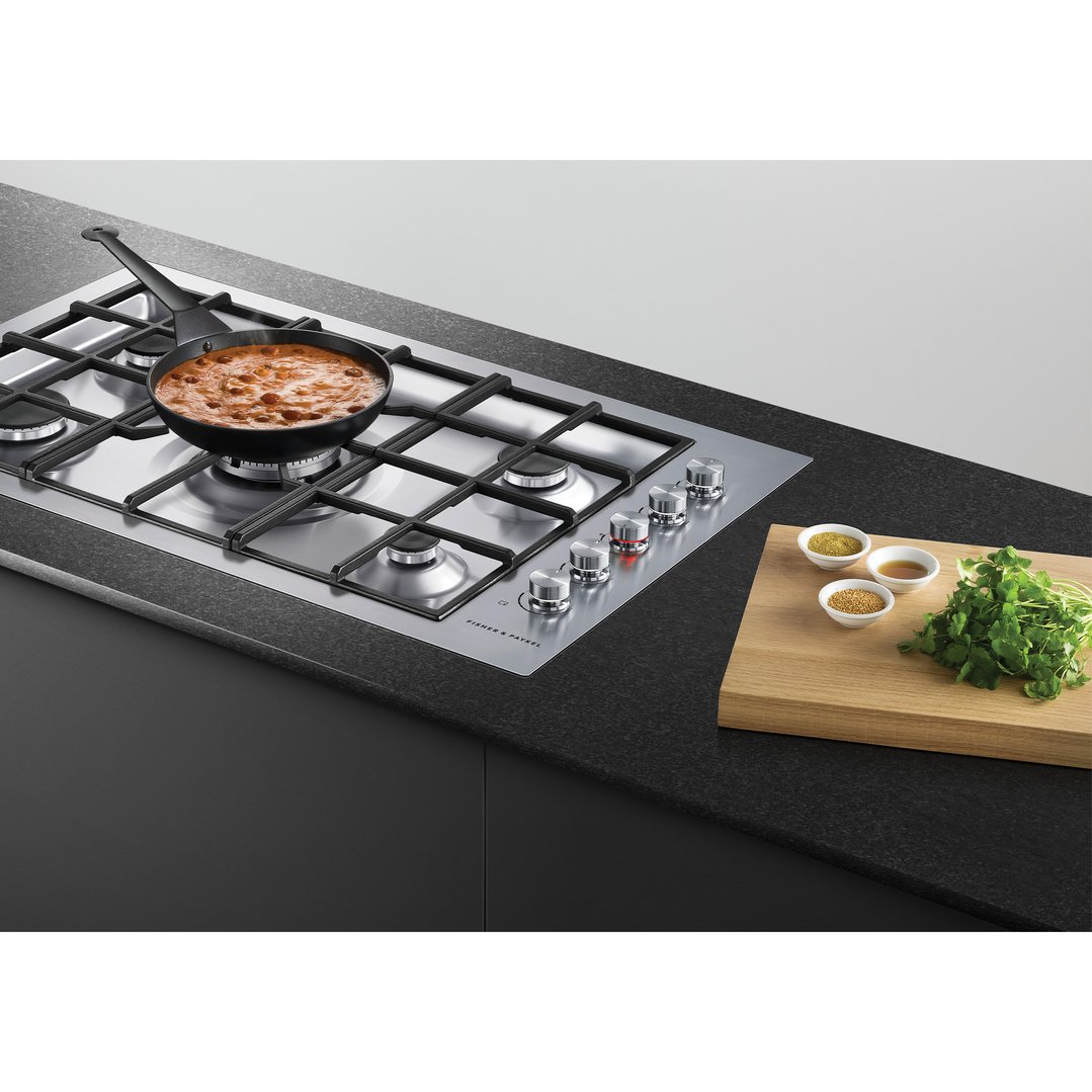 Gas cooktop with a pan of food cooking, spices, and herbs on a cutting board