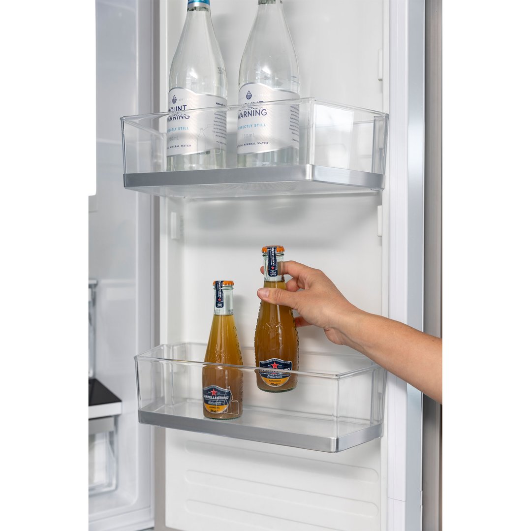 Hand placing a bottle into a clear bin inside a French door fridge