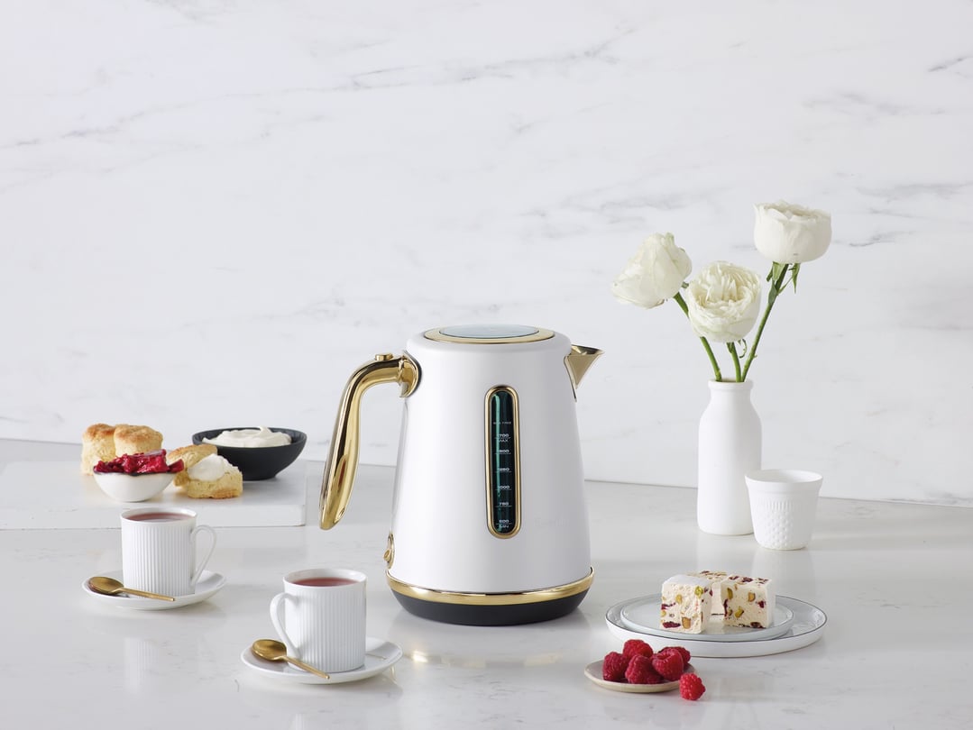 White and gold Breville kettle on a counter with tea, scones, and dessert