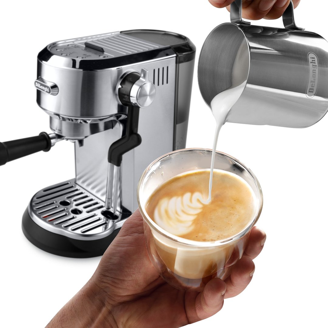 Hands pouring frothed milk into a coffee cup with a coffee machine in the background