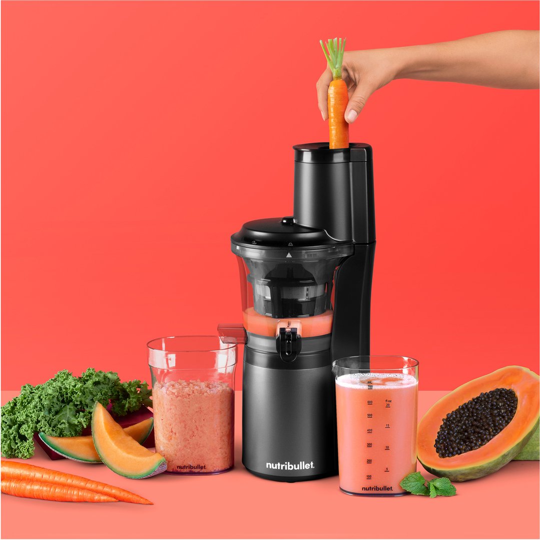 Hand placing a carrot into a NUTRiBULLET Slow Juicer with fruits and juice