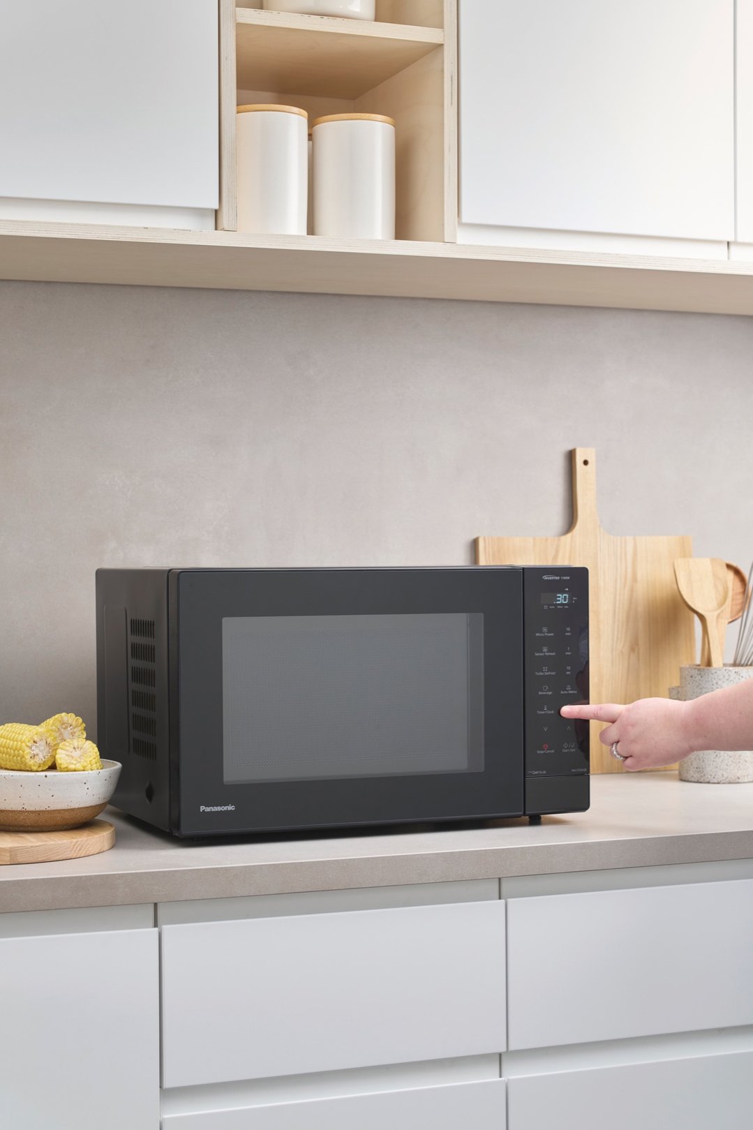 Hand pressing button on black Panasonic microwave on kitchen counter with corn