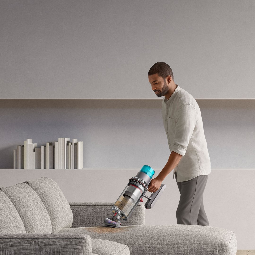 Man using a Dyson handstick vacuum to clean a sofa