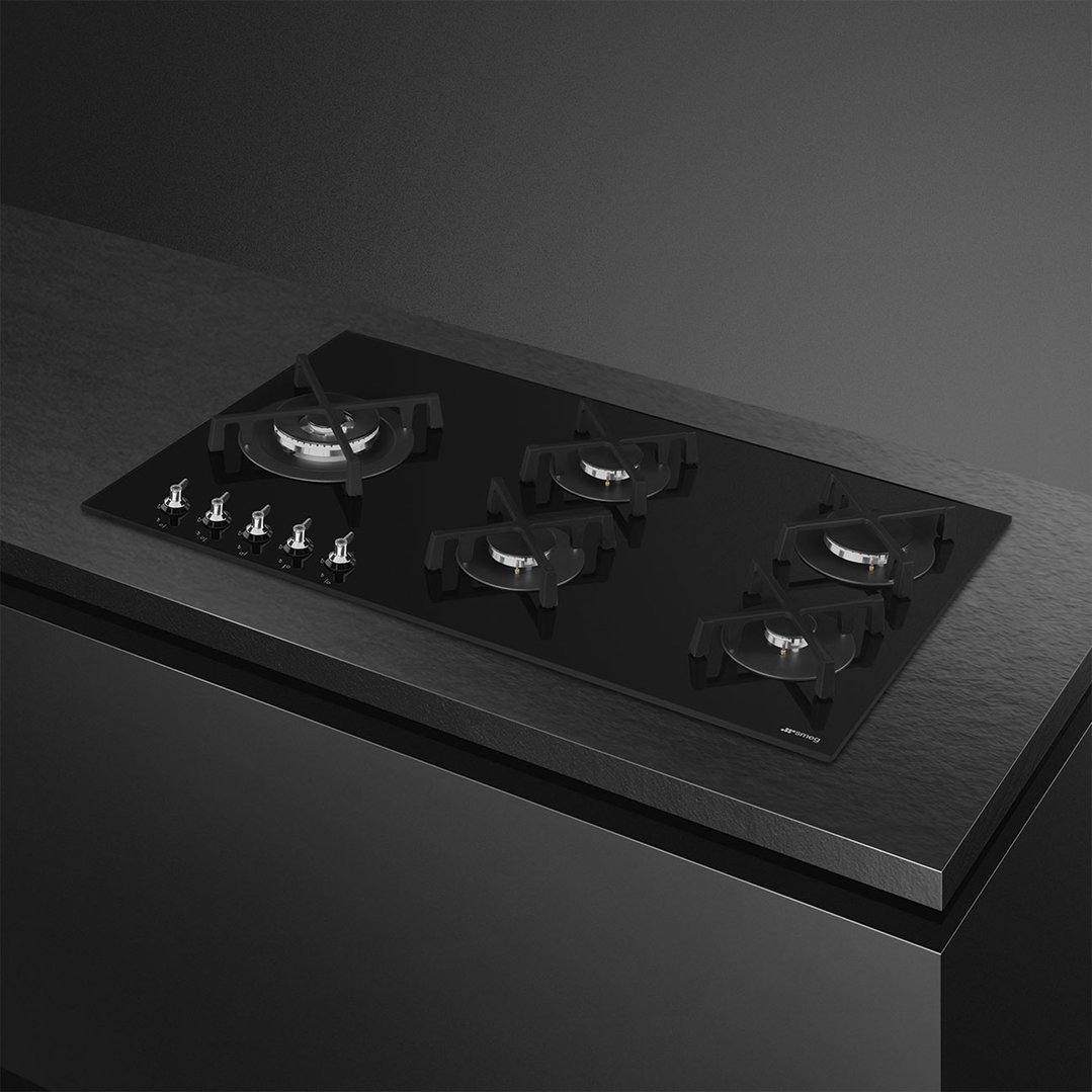 Black glass gas cooktop with five burners and controls on a dark countertop