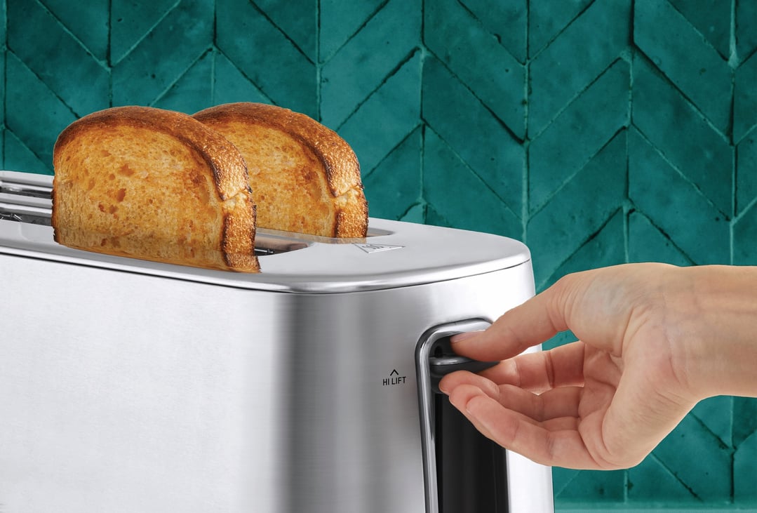 Hand pushing down lever on a stainless steel toaster with two slices of toast