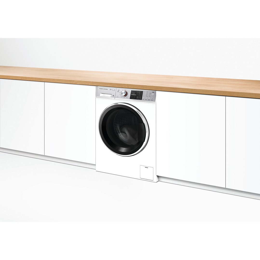 White Fisher & Paykel washing machine integrated into white cabinetry with a wooden countertop